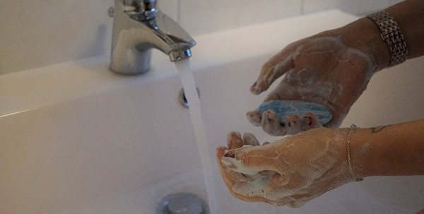 Pessoa lavando as mãos para cuidar do furo na orelha.